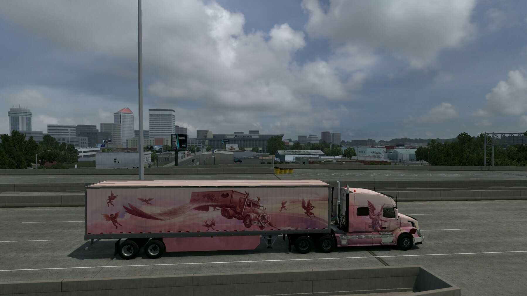 A pink semi-truck with decorative graphics is driving on a highway with a city skyline in the background.