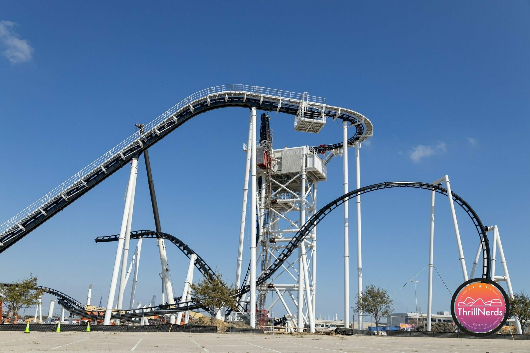 A looping roller coaster features steep inclines and twists against a clear blue sky.